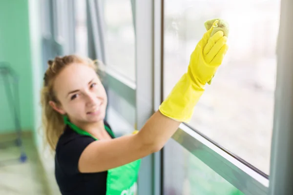 Улыбающаяся молодая женщина-работница чистит мыло на стеклянном окне с помощью скребка и тряпки — стоковое фото