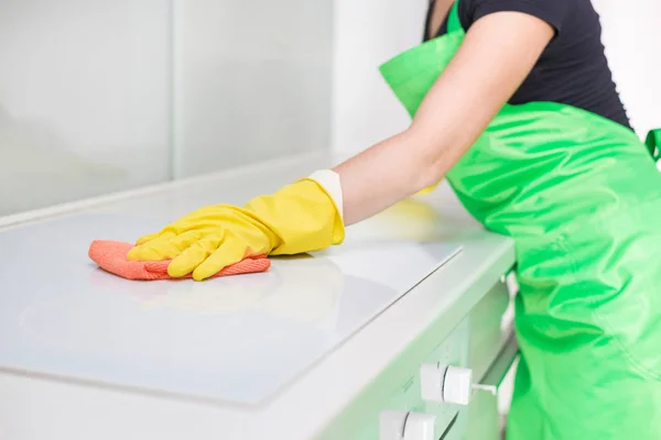 Gros plan des mains féminines en gants jaunes en caoutchouc nettoyant le panneau de la cuisinière à la cuisine de la maison. Maison, concept de ménage. service de nettoyage — Photo