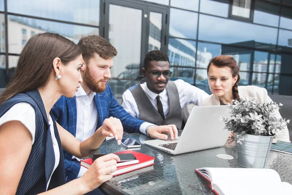 Grupo de hombres y mujeres de negocios diverso feliz equipo en formal se reunieron alrededor de la computadora portátil en la oficina brillante en el fondo de un edificio de vidrio — Foto de Stock