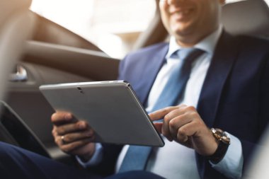 Genç işadamı bir arabanın arka koltuğunda otururken Tablet PC'yi kullanma. Beyaz erkek iş bir taksi ile yönetici ve dijital tablet bakarak.