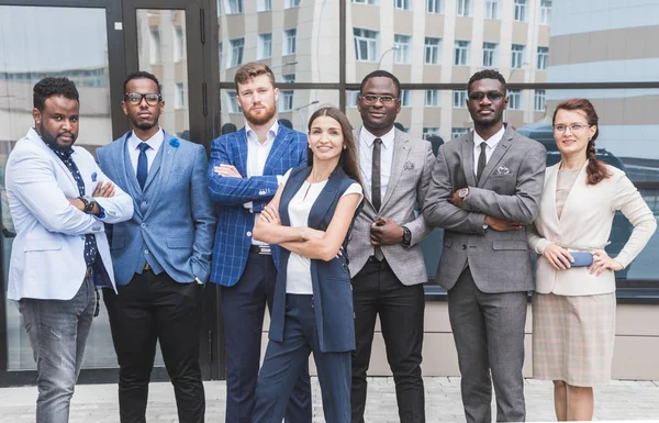 Successful company with happy workers. Men and women in business suits stand with their arms crossed against the background of skyscrapers