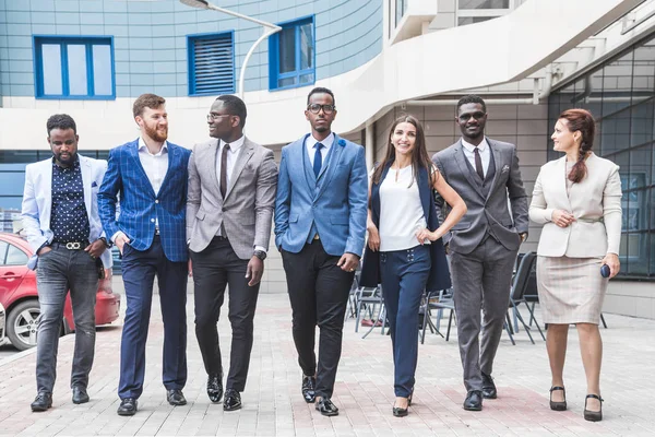 Successful company with happy workers. Men and women in business suits stand with their arms crossed against the background of skyscrapers