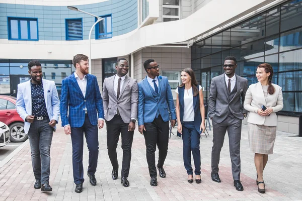 Successful company with happy workers. Men and women in business suits stand with their arms crossed against the background of skyscrapers