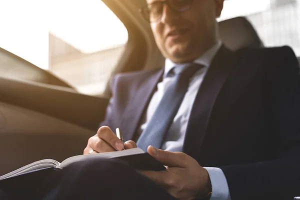 El hombre en el traje de trabajo escriben en el portátil con el portátil en el salón del automóvil caro con el interior de cuero — Foto de Stock