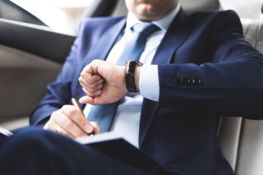 Pahalı bir araba ile deri iç salonda dizüstü bilgisayar ile bir iş takım elbise yazmak üstünde defter adam