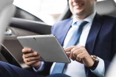 Genç işadamı bir arabanın arka koltuğunda otururken Tablet PC'yi kullanma. Beyaz erkek iş bir taksi ile yönetici ve dijital tablet bakarak.
