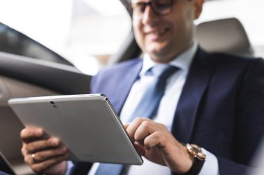 Genç işadamı bir arabanın arka koltuğunda otururken Tablet PC'yi kullanma. Beyaz erkek iş bir taksi ile yönetici ve dijital tablet bakarak.