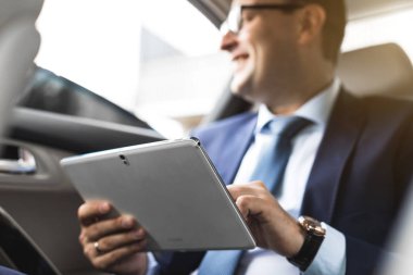 Genç işadamı bir arabanın arka koltuğunda otururken Tablet PC'yi kullanma. Beyaz erkek iş bir taksi ile yönetici ve dijital tablet bakarak.