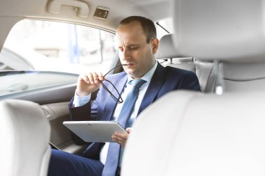 Genç işadamı bir arabanın arka koltuğunda otururken Tablet PC'yi kullanma. Beyaz erkek iş bir taksi ile yönetici ve dijital tablet bakarak.