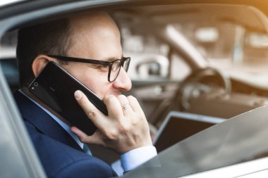 Cep telefonu üzerinde konuşurken ve bir arabanın arka koltuğunda otururken tablet pc kullanarak genç iş adamı. Beyaz erkek iş bir taksi ile yönetici ve dijital tablet bakarak.