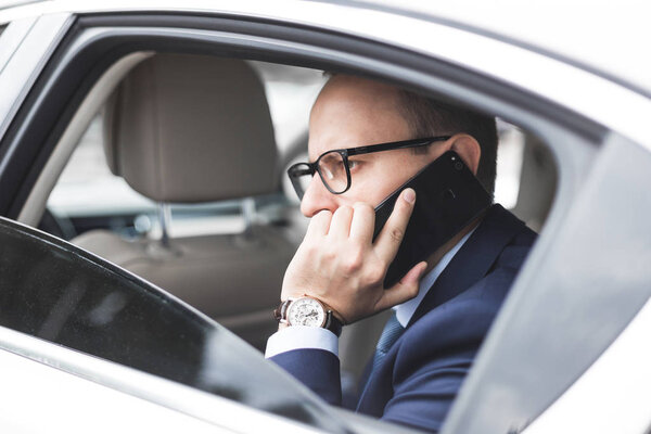 молодой успешный бизнесмен разговаривает по телефону сидя на заднем сиденье элитного автомобиля, переговоры и деловые встречи
