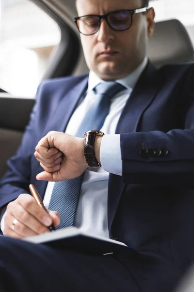 El hombre en el traje de trabajo escriben en el portátil con el portátil en el salón del automóvil caro con el interior de cuero — Foto de Stock