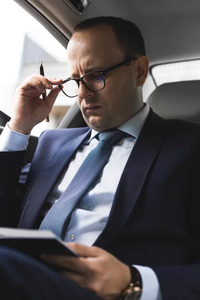 El hombre en el traje de trabajo escriben en el portátil con el portátil en el salón del automóvil caro con el interior de cuero — Foto de Stock