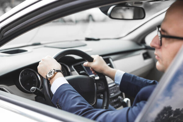 бизнесмен за рулём престижной машины держит в руках мобильный телефон. Быстрая жизнь
