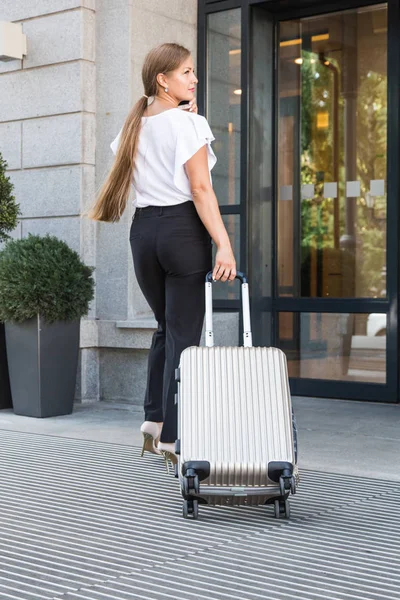 Una chica en un traje de negocios y gafas con una maleta en el fondo de un hotel caro. joven hermosa mujer eset equipaje — Foto de Stock