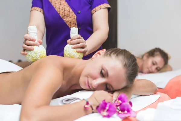 Две милые молодые женщины наслаждаются во время процедуры по уходу за кожей в спа. массаж и косметические процедуры в салоне красоты. розовая орхидея на переднем плане — стоковое фото