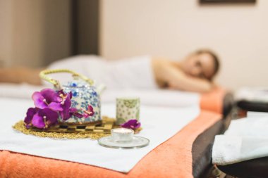 Genç güzel kız spa salonda. Kız bir gençleştirme işlemden sonra bir masaj için kanepede yatıyor. orkide ve bir çaydanlık ile yeşil çay Tay tarzında bir kompozisyonu