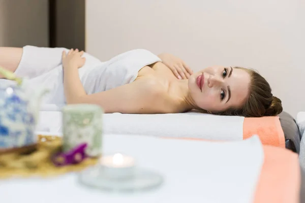 Jeune belle fille dans le salon de spa. La fille s'allonge sur le canapé pour un massage après une procédure de rajeunissement. une composition dans le style thaï avec une orchidée et une théière avec du thé vert — Photo