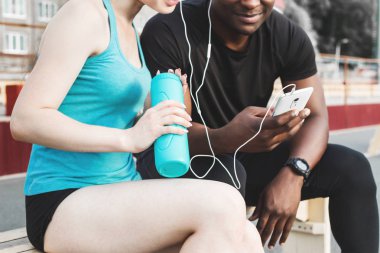 Bankta oturan ve sert sokak egzersiz oturum sonrası istirahat sporcular grubudur. Erkek ve kadın kentsel spor yapıyor. spor, müzik, dinlemek su içtikten sonra dinlenme