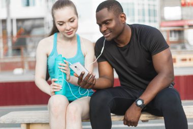 Bankta oturan ve sert sokak egzersiz oturum sonrası istirahat sporcular grubudur. Erkek ve kadın kentsel spor yapıyor. spor, müzik, dinlemek su içtikten sonra dinlenme