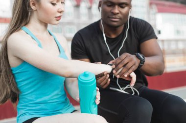 Bankta oturan ve sert sokak egzersiz oturum sonrası istirahat sporcular grubudur. Erkek ve kadın kentsel spor yapıyor. spor, müzik, dinlemek su içtikten sonra dinlenme