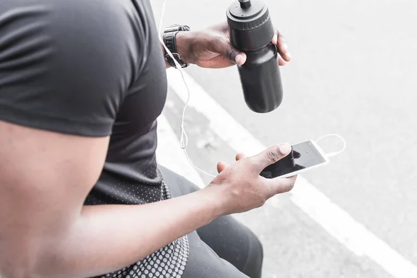 Young male jogger athlete training and doing workout outdoors in city. a black man resting after a workout and listening to music and watching a sports watch