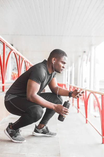 Young male jogger athlete training and doing workout outdoors in city. a black man resting after a workout and listening to music and watching a sports watch