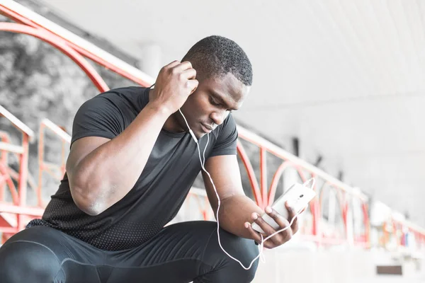 Young male jogger athlete training and doing workout outdoors in city. a black man resting after a workout and listening to music and watching a sports watch