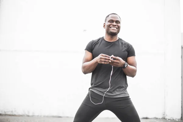 Smiling Young male jogger athlete training and doing workout outdoors in city. a black man resting after a workout and listening to music and watching a sports watch. free copyspace for text