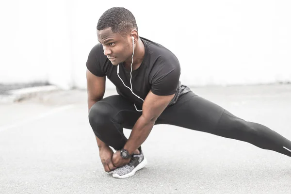 Young male jogger athlete training and doing workout outdoors in city. a black man resting after a workout and listening to music and watching a sports watch. free copyspace for text
