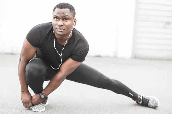 Young male jogger athlete training and doing workout outdoors in city. a black man resting after a workout and listening to music and watching a sports watch. free copyspace for text