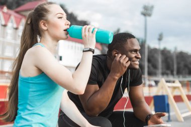Bankta oturan ve sert sokak egzersiz oturum sonrası istirahat sporcular grubudur. Erkek ve kadın kentsel spor yapıyor. spor, müzik, dinlemek su içtikten sonra dinlenme