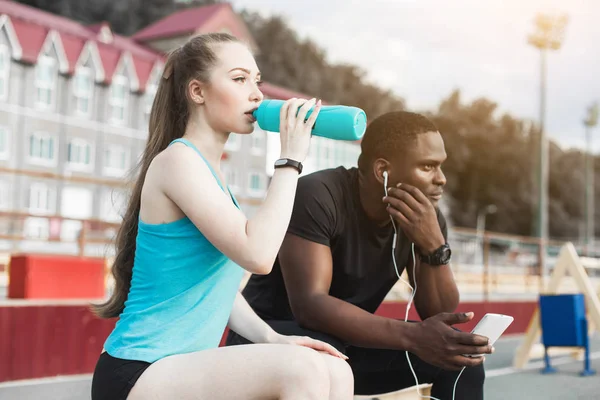 Csoport sportolók ül a padon, és pihenő-ülés kemény utcai edzés után. Férfi és nő városi sportolás. pihenő után a sport, veszelyes, vizet inni — Stock Fotó