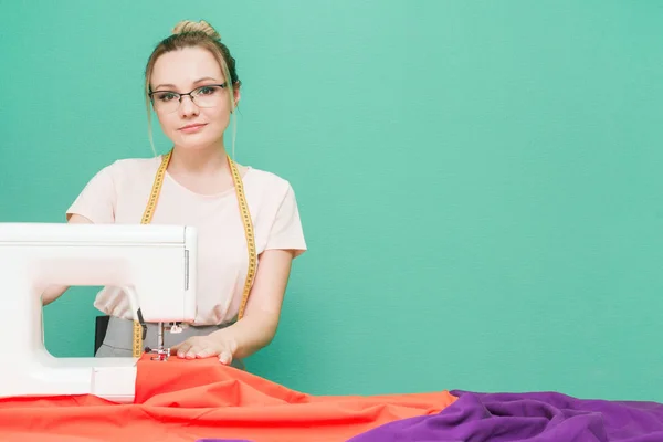 Sewing workshop. Seamstress at work. Young woman working with sewing machine on a colored background