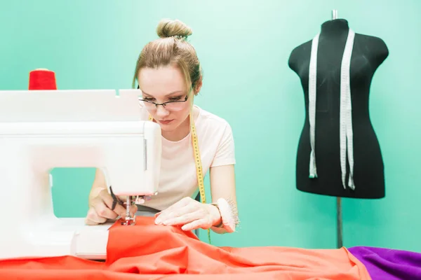 Nähwerkstatt. Näherin bei der Arbeit. junge Frau arbeitet mit Nähmaschine auf farbigem Hintergrund — Stockfoto