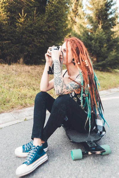 Young girl with tattoos and dreadlocks photographs vintage camera in the park — Stock Photo, Image