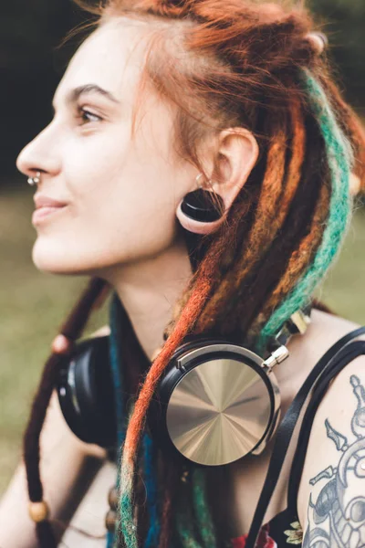 Chica joven con tatuaje y rastas escuchando música en el parque — Foto de Stock