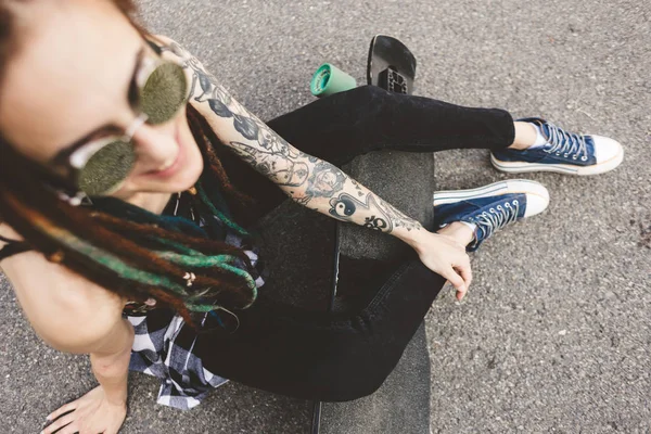Молода дівчина з татуюванням та дредлоками сидить у парку — стокове фото
