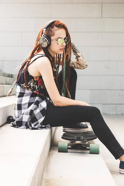 Chica joven con tatuaje y rastas escuchando música mientras se sienta en los escalones —  Fotos de Stock