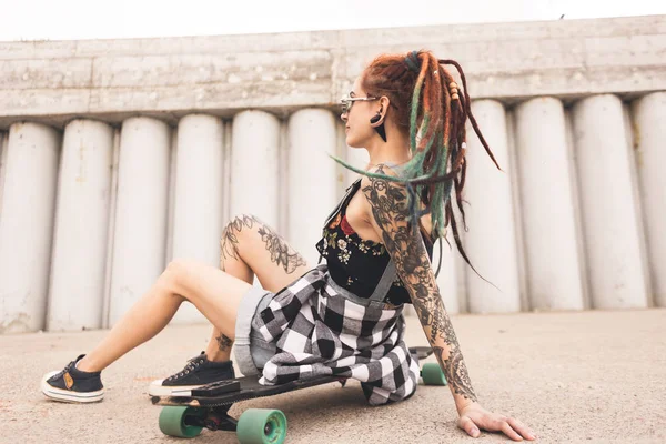 Jong meisje met tattoo en zittend op een longboard op de achtergrond van de betonstructuur dreadlocks — Stockfoto