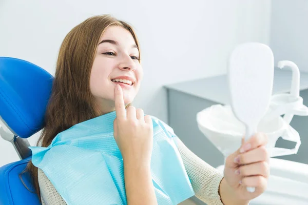 Clinica dentistica. Accoglienza, esame del paziente. Cura dei denti. Giovane ragazza sorridente, guardarsi allo specchio dopo un controllo dentale al suo dentista — Foto Stock