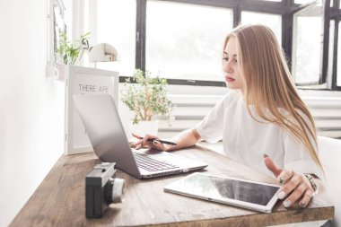 Evde bir dizüstü ve tablet çalışan genç iş kadını. Yaratıcı İskandinav tarzı çalışma alanı