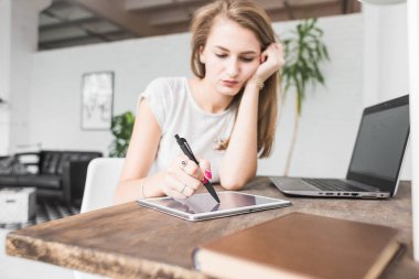 Evde çalışan genç iş kadını ve berabere tablette. Yaratıcı İskandinav tarzı çalışma alanı