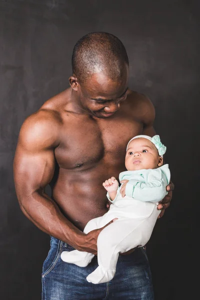 Muscular African American man holding a child against a black wall — Stock Photo, Image