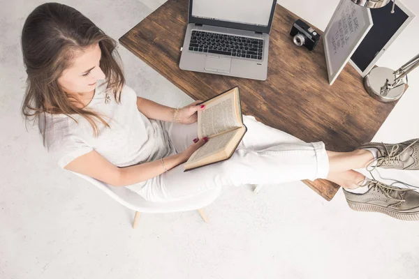 Joven mujer de negocios trabajando en casa y leyendo un libro con las piernas sobre la mesa. Espacio de trabajo de estilo escandinavo creativo. # Wiew from above — Foto de Stock