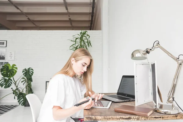 Νεαρή γυναίκα που εργάζονται στο σπίτι πίσω από ένα φορητό υπολογιστή και tablet. Δημιουργική σκανδιναβικό στυλ χώρου εργασίας — Φωτογραφία Αρχείου