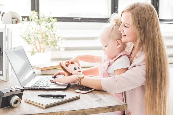 Joven mujer de negocios que trabaja en casa detrás del portátil con un niño pequeño. Espacio de trabajo de estilo escandinavo creativo. Trabajos sobre el permiso de maternidad — Foto de Stock