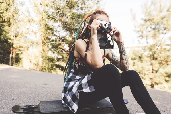 young girl with tattoos and dreadlocks photographs vintage camera in the park