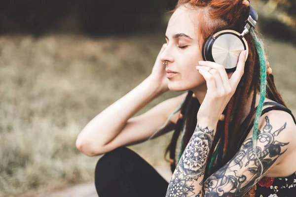 Chica joven con tatuaje y rastas escuchando música en el parque — Foto de Stock