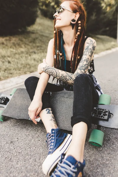 Молода дівчина з татуюванням та дредлоками сидить у парку — стокове фото
